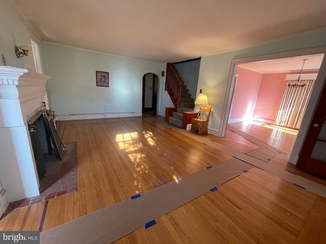 unfurnished living room featuring arched walkways, stairway, an inviting chandelier, a brick fireplace, and wood finished floors