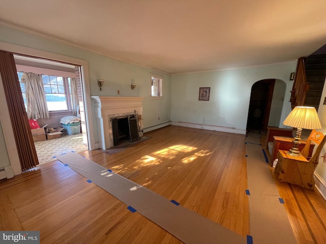 unfurnished living room with arched walkways, a baseboard heating unit, ornamental molding, a fireplace with flush hearth, and wood finished floors