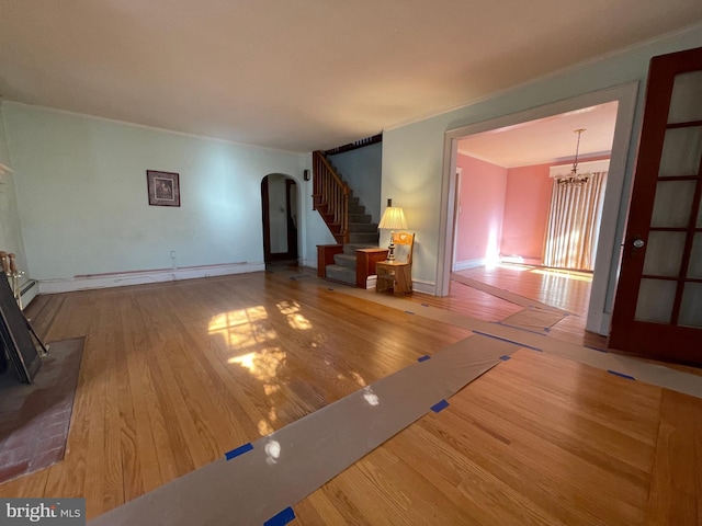 unfurnished living room with arched walkways, stairway, an inviting chandelier, and hardwood / wood-style flooring