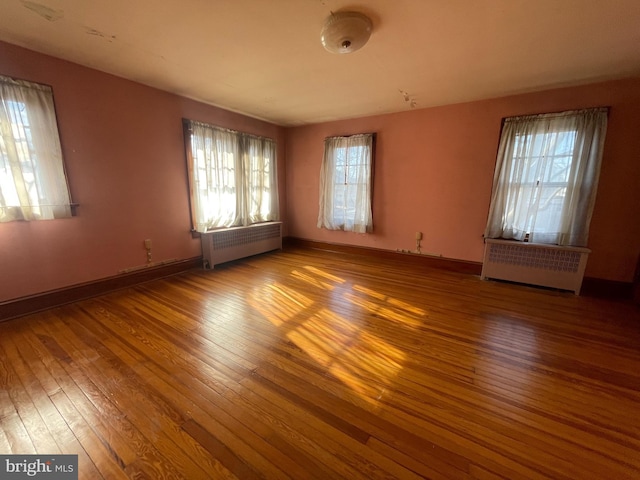 empty room with baseboards, radiator heating unit, and hardwood / wood-style flooring