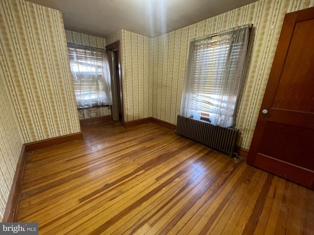 empty room featuring radiator, wallpapered walls, baseboards, and hardwood / wood-style floors