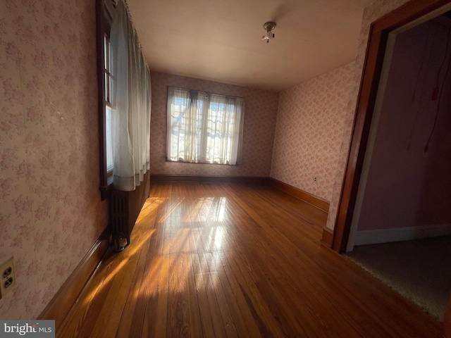 unfurnished bedroom featuring baseboards, hardwood / wood-style floors, and wallpapered walls