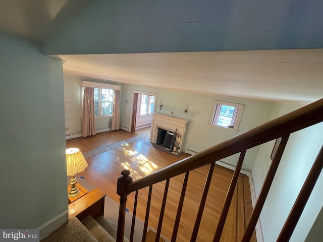 staircase with a fireplace, wood finished floors, a baseboard radiator, and baseboards