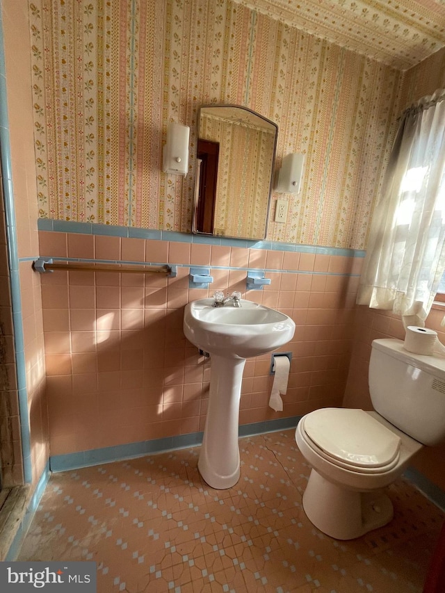 bathroom featuring toilet, wallpapered walls, tile walls, and wainscoting