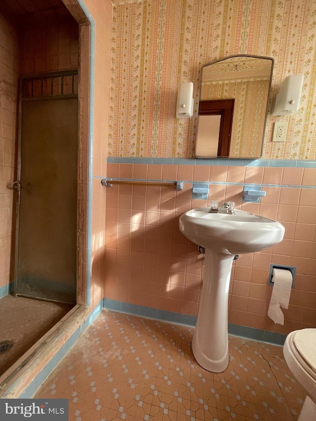 full bath featuring wallpapered walls, a stall shower, wainscoting, toilet, and tile walls