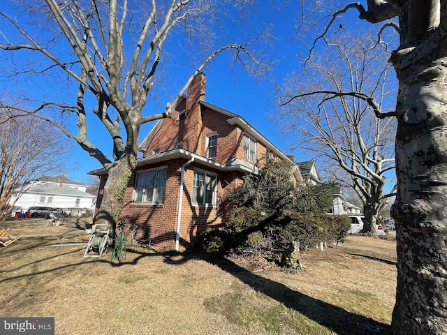 view of property exterior with brick siding, a lawn, and a chimney