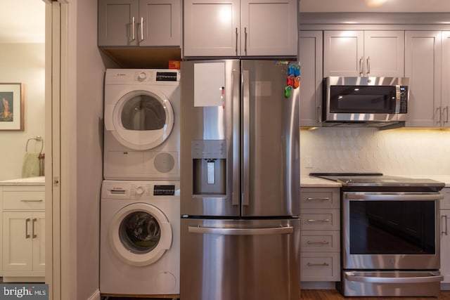 kitchen featuring stainless steel appliances, stacked washer / drying machine, light countertops, and tasteful backsplash