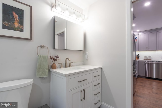 bathroom with toilet, wood finished floors, vanity, and baseboards