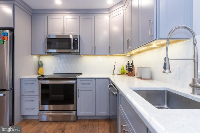 kitchen with dark wood-style floors, stainless steel appliances, gray cabinetry, a sink, and light stone countertops