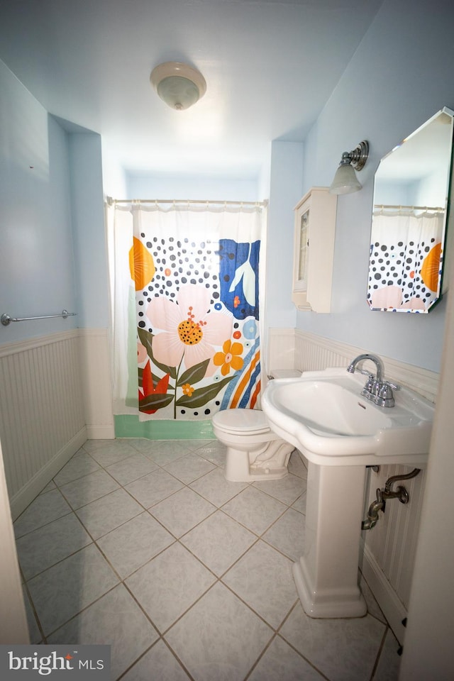 full bathroom with curtained shower, wainscoting, toilet, and tile patterned floors