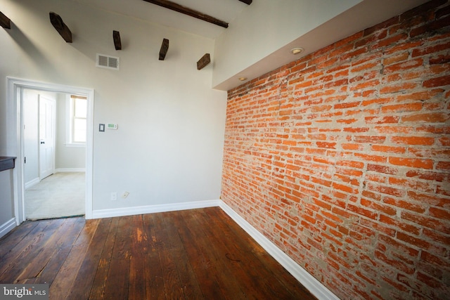 spare room featuring visible vents, dark wood finished floors, baseboards, brick wall, and a high ceiling