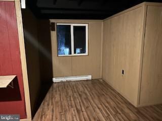 unfurnished room featuring wood finished floors, baseboard heating, and a barn door