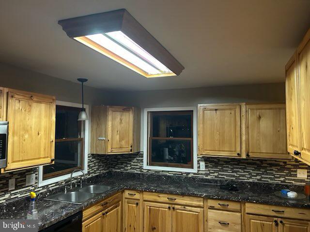 kitchen with dark stone counters, pendant lighting, stainless steel microwave, and a sink