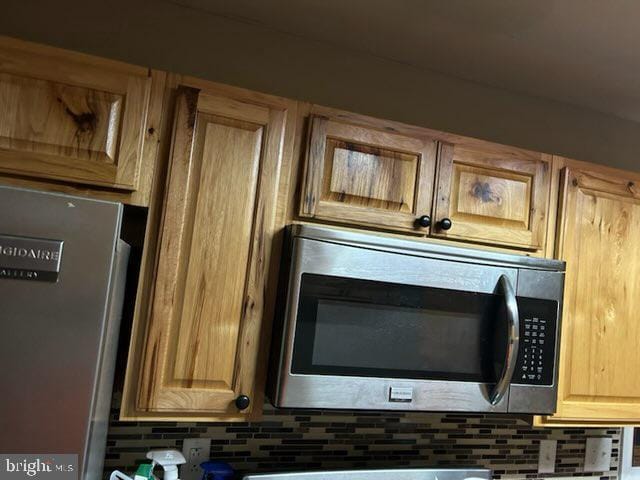 interior details featuring tasteful backsplash, stainless steel microwave, and refrigerator