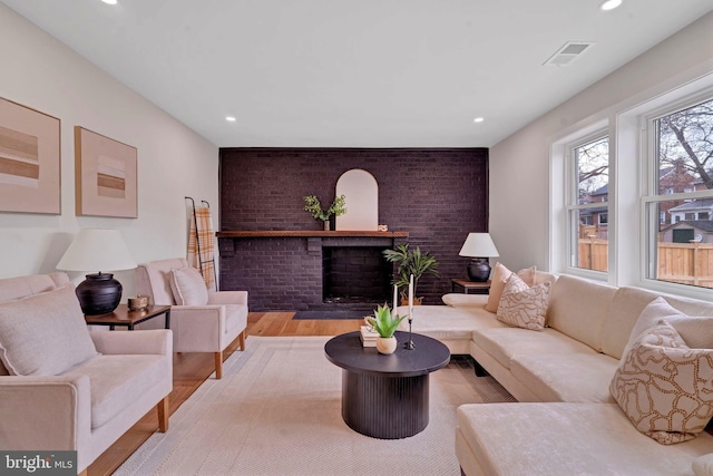 living room featuring recessed lighting, an accent wall, visible vents, a brick fireplace, and light wood finished floors