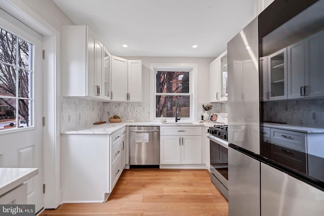 kitchen with stainless steel appliances, white cabinetry, glass insert cabinets, and a sink