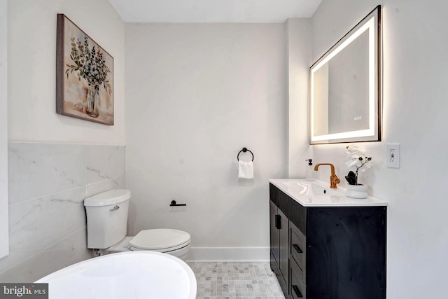 bathroom featuring toilet, baseboards, tile walls, and vanity