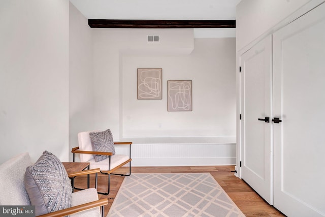 sitting room with visible vents, light wood-type flooring, and beam ceiling