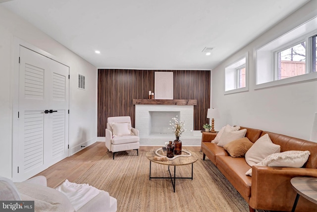 living room featuring a fireplace, recessed lighting, visible vents, light wood-style flooring, and wood walls