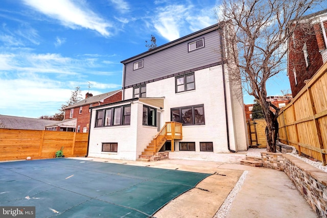 rear view of house with a fenced in pool, brick siding, fence, and a patio