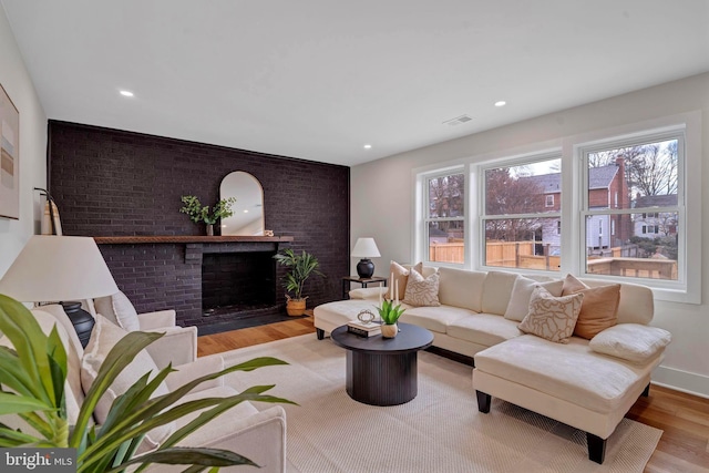 living room featuring visible vents, brick wall, light wood-type flooring, a fireplace, and recessed lighting