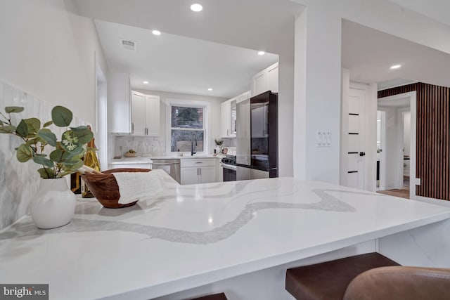 kitchen with a peninsula, appliances with stainless steel finishes, visible vents, and white cabinets