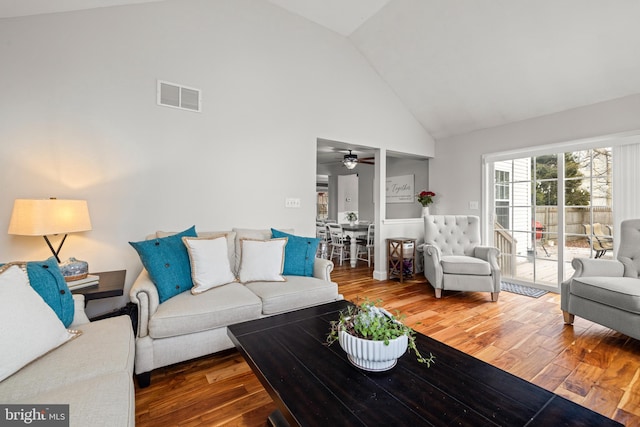 living area featuring high vaulted ceiling, visible vents, and wood finished floors