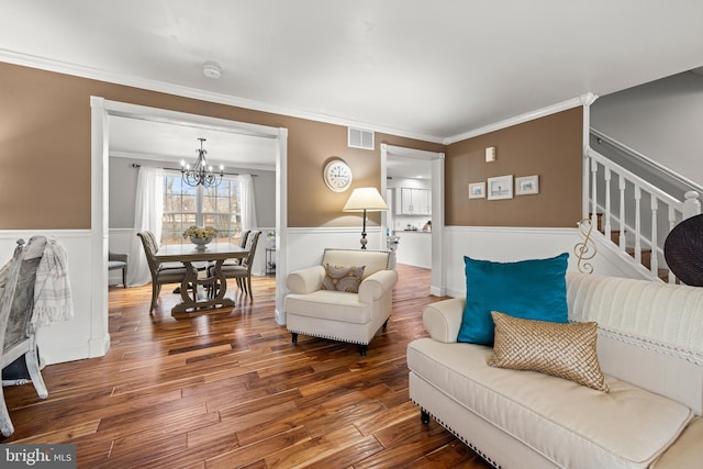 living area featuring a wainscoted wall, wood finished floors, visible vents, stairway, and crown molding