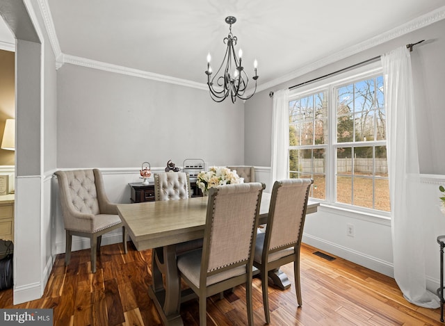 dining space featuring crown molding, visible vents, an inviting chandelier, wood finished floors, and baseboards