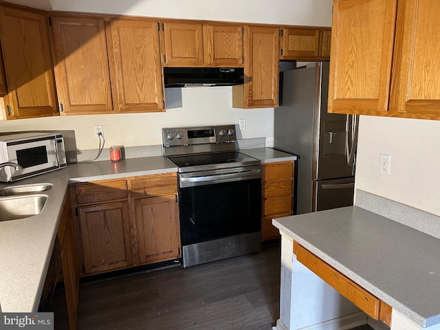 kitchen featuring dark wood-style flooring, brown cabinets, appliances with stainless steel finishes, a sink, and under cabinet range hood