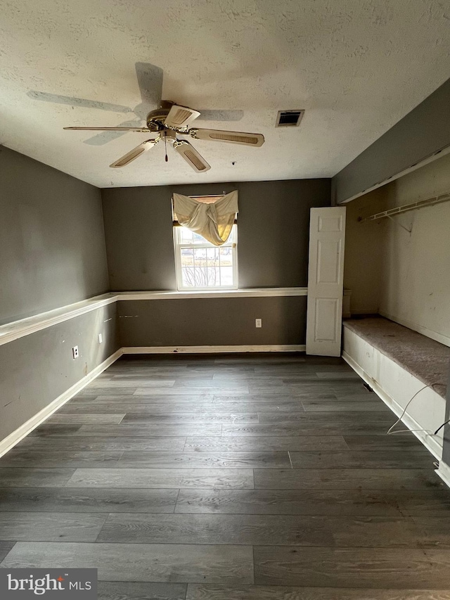 unfurnished bedroom featuring a textured ceiling, dark wood-style flooring, visible vents, and baseboards