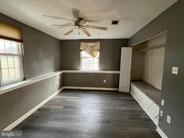 unfurnished bedroom featuring a textured ceiling, multiple windows, visible vents, and dark wood-type flooring