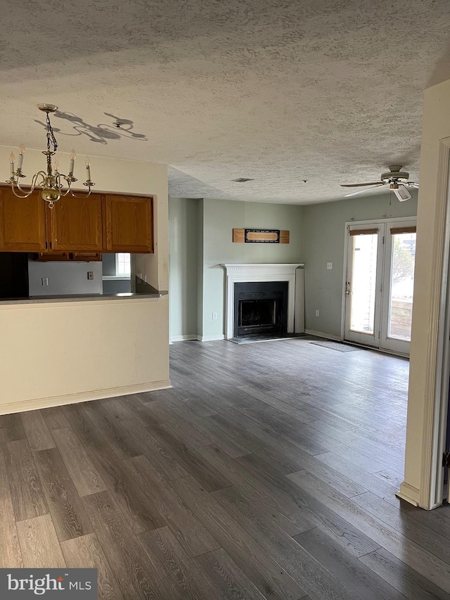 unfurnished living room featuring a textured ceiling, ceiling fan with notable chandelier, a fireplace, wood finished floors, and baseboards