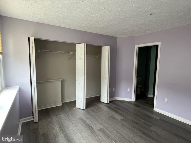 unfurnished bedroom with connected bathroom, a textured ceiling, baseboards, and dark wood-type flooring