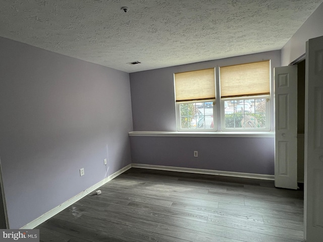 empty room featuring a textured ceiling, wood finished floors, visible vents, and baseboards