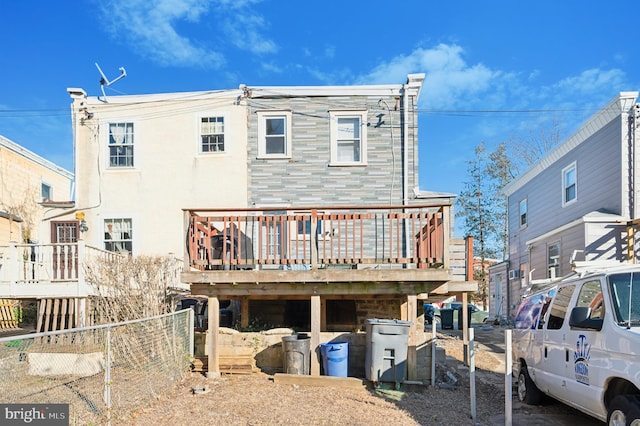 rear view of house with fence, a wooden deck, and stucco siding