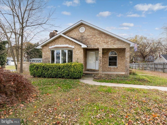 view of front facade featuring a front yard, a chimney, fence, and brick siding