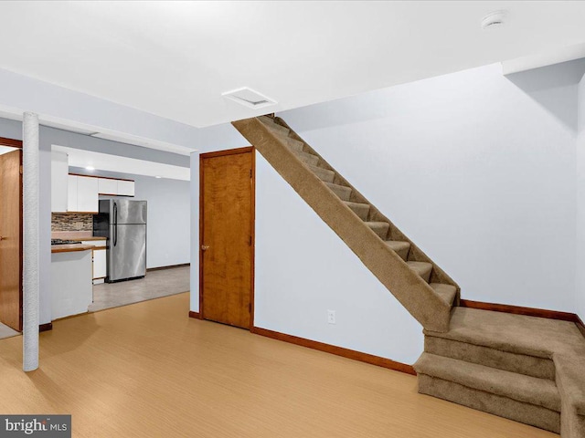 unfurnished living room with stairs, light wood finished floors, visible vents, and baseboards