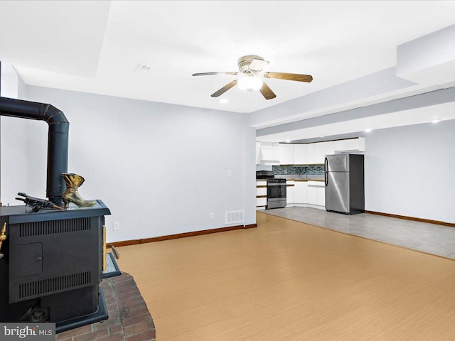 workout room featuring wood finished floors, visible vents, baseboards, a ceiling fan, and a wood stove