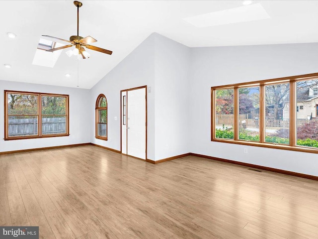 unfurnished living room with ceiling fan, light wood finished floors, a skylight, and a healthy amount of sunlight