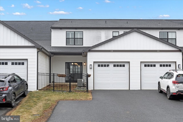 view of front of house with driveway, roof with shingles, an attached garage, central AC, and board and batten siding