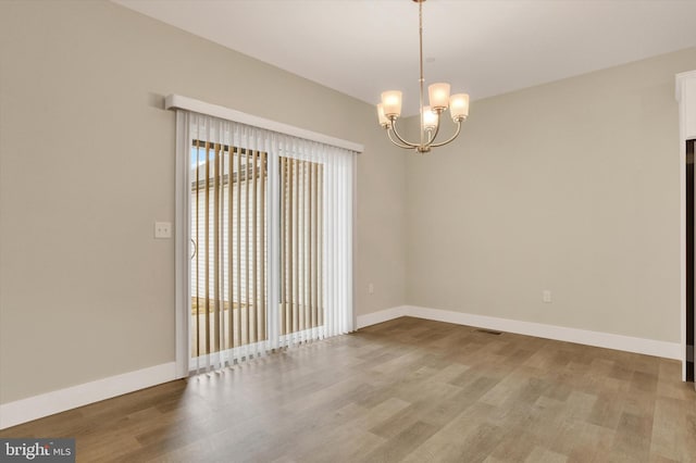 spare room with a notable chandelier, wood finished floors, and baseboards