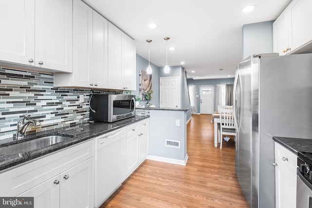 kitchen featuring stainless steel appliances, hanging light fixtures, white cabinets, a sink, and dark stone countertops