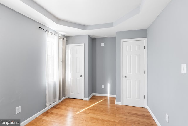 unfurnished bedroom with baseboards, a raised ceiling, and wood finished floors