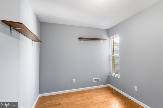 empty room with light wood finished floors, visible vents, and baseboards