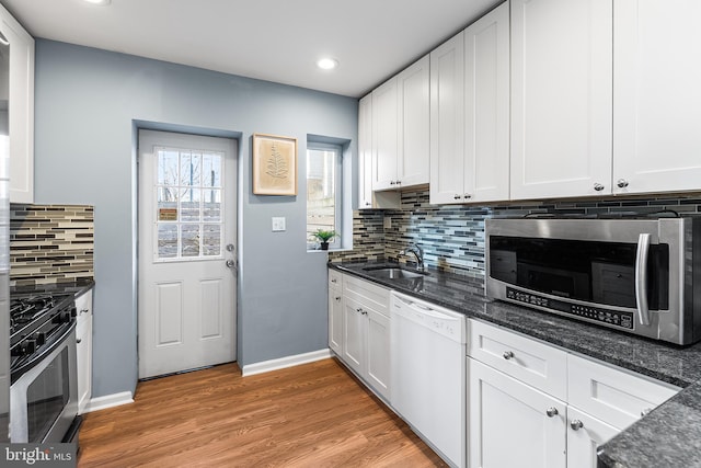 kitchen with light wood finished floors, dark stone counters, stainless steel appliances, white cabinetry, and a sink