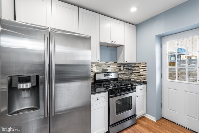 kitchen with stainless steel appliances, white cabinetry, light wood-style floors, backsplash, and dark stone counters