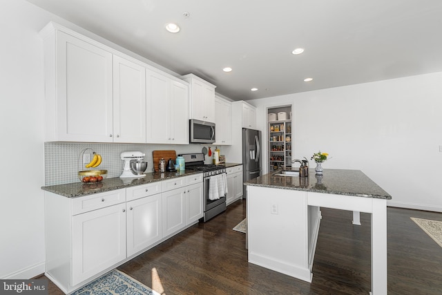 kitchen with dark wood-style flooring, a center island with sink, appliances with stainless steel finishes, white cabinets, and dark stone countertops