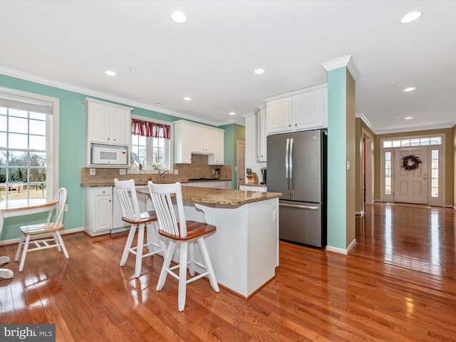 kitchen with freestanding refrigerator, white cabinets, a kitchen island, and white microwave