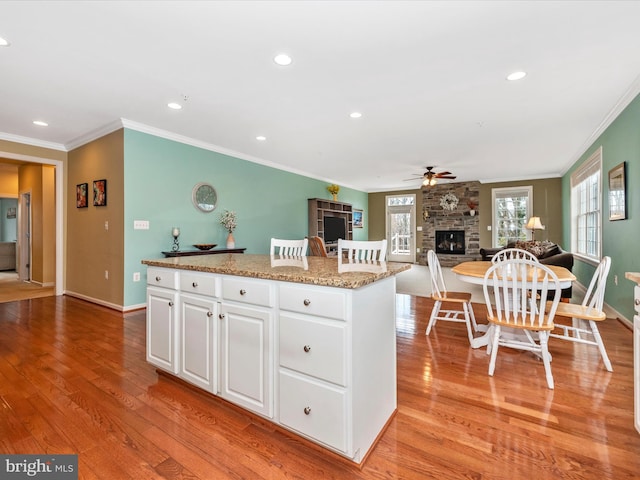 kitchen featuring a stone fireplace, white cabinetry, light wood-style floors, open floor plan, and a center island